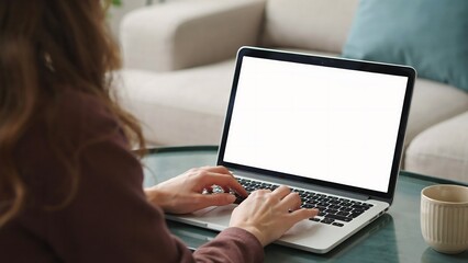 Fototapeta premium Young woman working on a laptop with a blank white screen at home