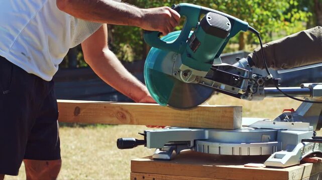 Man operating sliding miter saw outdoors cutting a wood beam