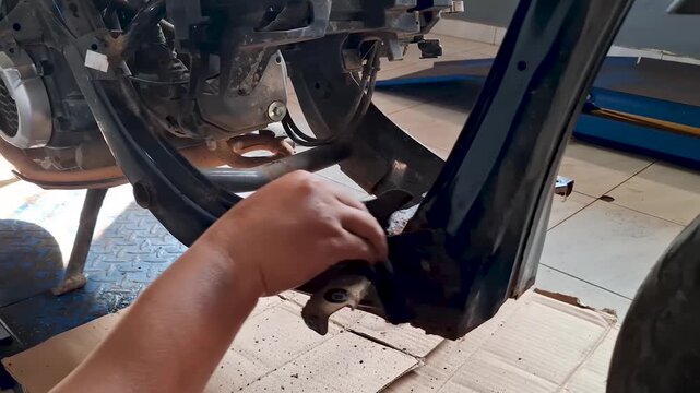 Close-up of a mechanic's hands wiping down and cleaning a dirty motorcycle chassis frame with a cloth during maintenance service in a garage repair shop.