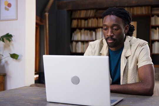 African American man sitting at wooden table working on silver laptop in home study, copy space
