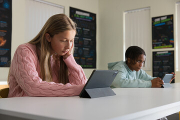 Teen students at table using tablet in folio, handheld tablet, girl in pink sweater © WavebreakMediaMicro