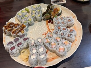 The image shows a large decorative platter arranged with an assortment of various maki sushi rolls, pickled ginger, and wasabi.Sushi Varieties IncludedCalifornia rolls with crab, avocado, and cucumber © Sandy Kitten