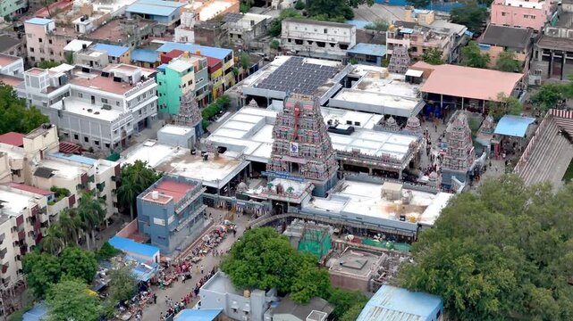 Wide overhead aerial view of Vadapalani Murugan Temple in Chennai, capturing multiple ornate gopurams, the adjacent temple tank, surrounding buildings, roads, and people moving around the busy temple.