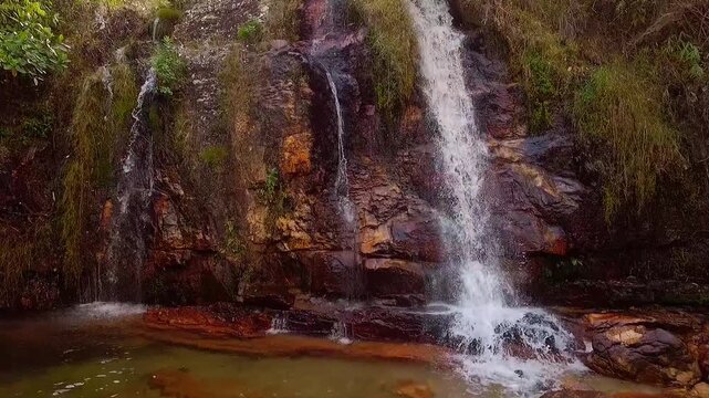 Loquinhas Waterfall cascades over layered rock into a clear pool amid Cerrado vegetation in Alto Paraiso de Goias, Goias, Brazil, extreme close-up FPV descent.