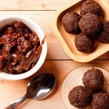 Chocolate brigadeiro with a creamy texture and chocolate sprinkle coating, presented on a bamboo tray on a wooden table.