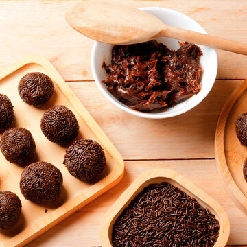 Handmade Brazilian chocolate brigadeiro coated in sprinkles, presented on a bamboo tray on a wooden table.