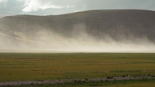 Sand storm moving by wind on grass field like wall with mountains background, 4k slow motion footage environment concept b roll shot.