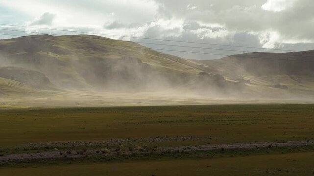 Sand storm moving by wind on grass field like wall with mountains background, 4k slow motion footage environment concept b roll shot.
