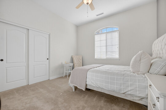 Bright neutral bedroom with window blinds, ceiling fan, tufted headboard, neatly made plush bed calm