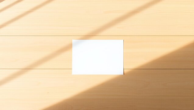 Blank white paper card mockup on a light wooden table with soft sunlight shadows