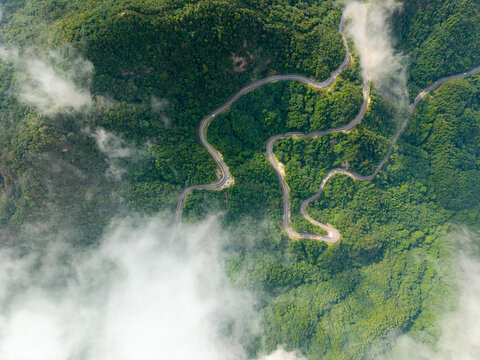 A winding road snakes through the lush green mountains of the Dabie Shan range in Hubei province located in central China as seen from an aerial view