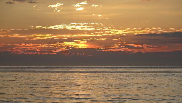 Bright Sun Rays Breaking Through Ocean Clouds at Sunrise.
Vibrant sunlight radiating through a thick layer of sky clouds over the tranquil sea at sunrise.
