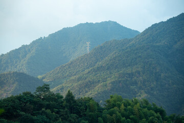 A tall electricity transmission tower stands on the green slopes of the Dabie Mountains in Hubei province of China under a clear sky © AS_SleepingPanda