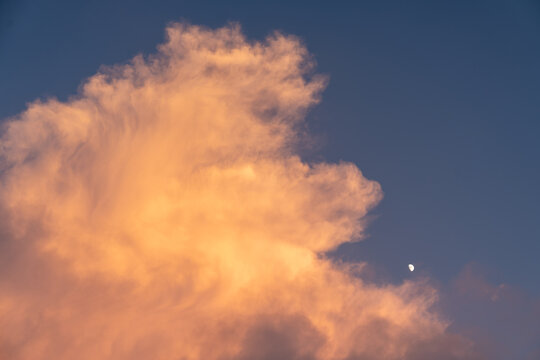 A beautiful view of golden sunset clouds drifting over the Dabie Mountains in Hubei Province of China with a small moon visible in the clear blue sky
