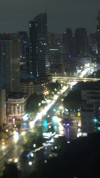 Vertical timelapse follows morning daylight arriving over avenue traffic and high rise skyscrapers as night ends in Shanghai, China, with tilt shift blur