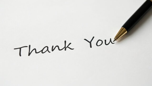 A black pen writes thank you in cursive handwriting on white paper. Ideal for gratitude greeting cards and appreciation messages.