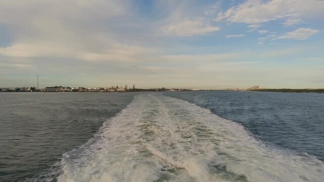 Boat speeds across calm waters, leaving frothy wake behind. Sky glows with soft clouds, distant land barely visible. No people seen, just serene motion on open water. Ideal for travel, vacation