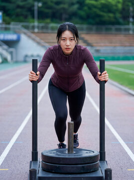 Determined woman pushing weight sled on running track, great for high-intensity workout ads or sports blog.
