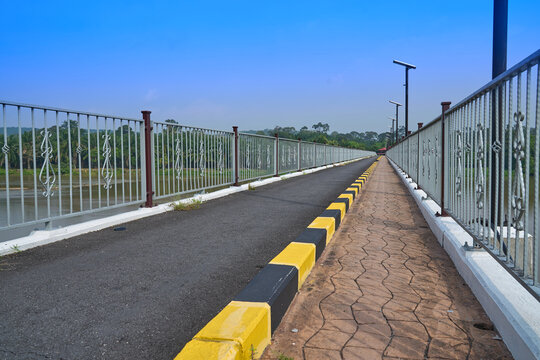 Pedestrian bridge walkway with metal railing and yellow curb railailing pavement infrastructure construction engineering transportation crossing landscape greenery perspective concrete