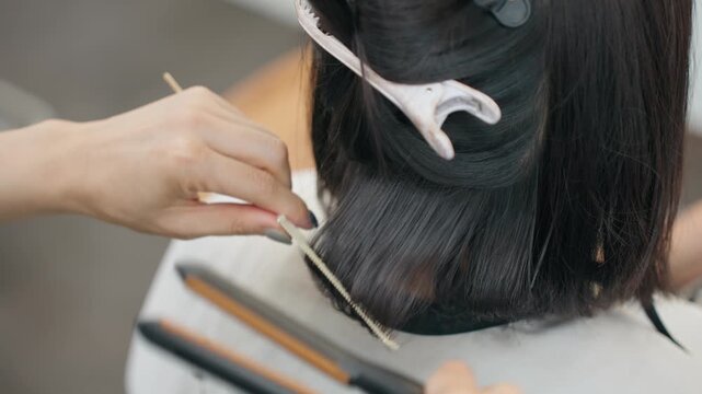 Hairdresser sections dark hair with clip and comb while using flat iron to style ends into smooth curl