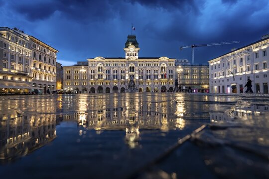 Illuminated square Piazza Unit&agrave; d'Italia, Town Hall, Palazzo Communale, with reflection, dramatic clouds, blue hour, old town, Trieste, Friuli-Venezia Giulia region, Italy