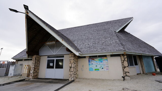 A daytime view of the small passenger terminal at Fakarava Airport in French Polynesia, showcasing its distinctive multi-tiered shingle roof, stone pillars, and welcoming island design