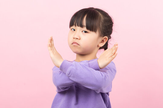 Serious little girl showing a cross sign with her arms as a gesture of refusal.