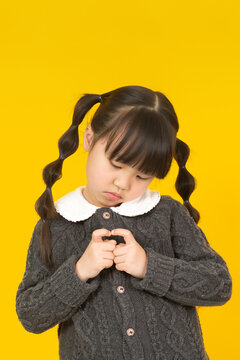 Shy and anxious little girl looking down while nervously playing with her fingers.