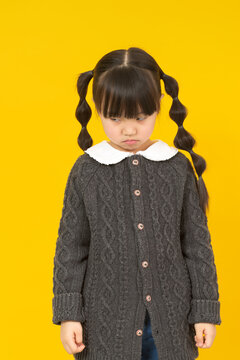 Sad and unhappy little girl looking down with a pouty disappointed face expression.
