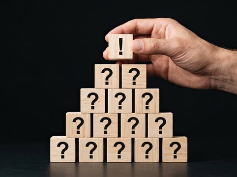Hand placing an exclamation block atop a pyramid of question blocks ideal for business strategy symbolizing clarity problem solving and answers