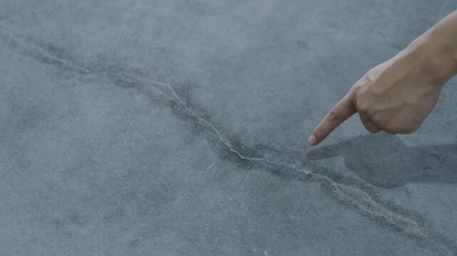 Hand Inspecting Crack in Concrete Floor