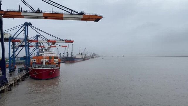 Wide view of a container port with cargo cranes beside calm water on an overcast day.