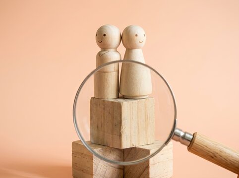 Wooden couple figures under magnifying glass suitable for HR hiring and dating content symbolizing candidate search match focus and analysis