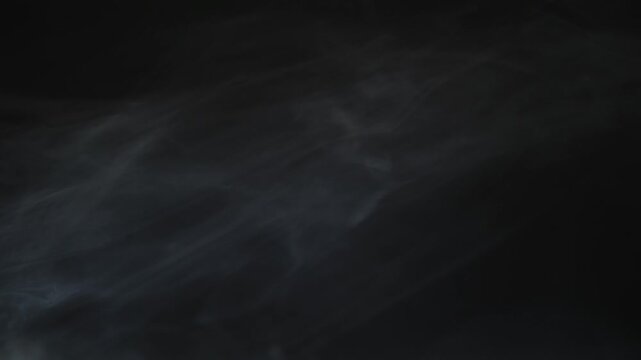 Atmospheric white smoke drifting slowly across dark black background in cinematic slow motion footage.