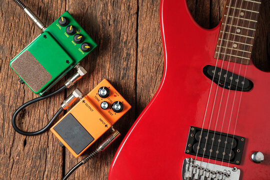 Red Electric Guitar and Two Effects Pedals on Rustic Wooden Background.