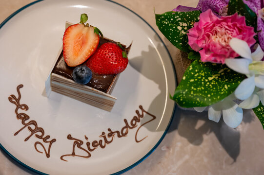 Chocolate birthday cake with fresh strawberries, blueberries, and flowers on a plate.