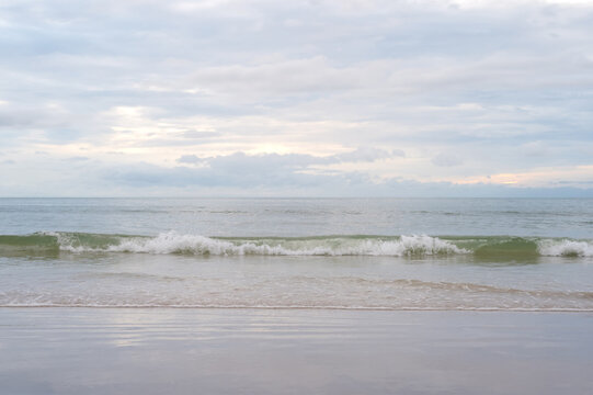 Gentle waves rolling onto a sandy beach under a cloudy sky.