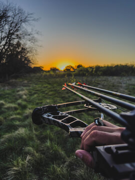 Archer holding a compound bow and arrows against a scenic landscape at sunrise during an outdoor archery adventure.