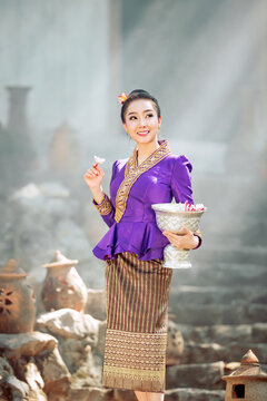 Young Laotian woman in traditional purple dress holding a silver bowl with flowers for a Buddhist temple offering in Laos.