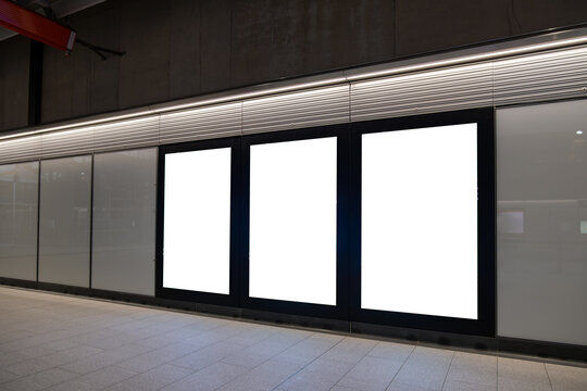 Three blank vertical billboard lightboxes mounted side-by-side along a modern underground subway or train station platform wall. A clean display mockup space. Copy space for commercial advertisement.