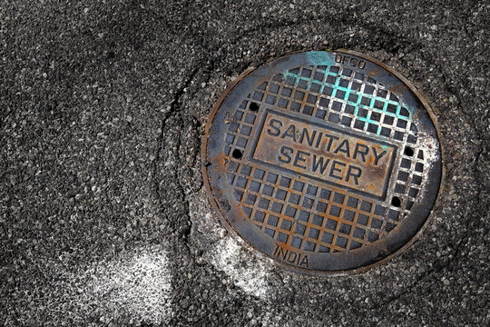 Sewer Man Hole Cover or Manhole Lid on Asphalt Worn Old and Rusty with Paint