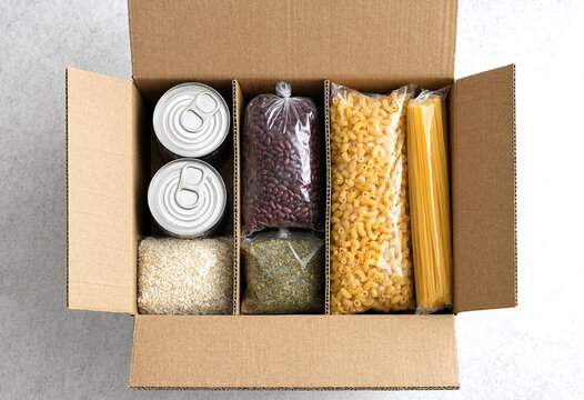 Open cardboard box filled with various dry food items including pasta rice beans and canned goods