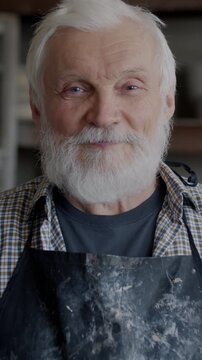 Slow motion portrait of senior man in apron standing in pottery studio smiling looking at camera. Small business and experienced artisans concept.