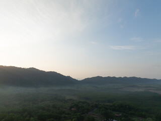 Aerial view of misty tropical forest and mountain ridges at sunrise, with morning light over green rural valley and blue sky. Nature, travel and environmental, conservation, climate and travel themes. © Fahroni
