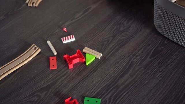 Colorful Wooden And Plastic Train Pieces On Dark Floor, Closeup Texture Near Gray Basket, Scattered