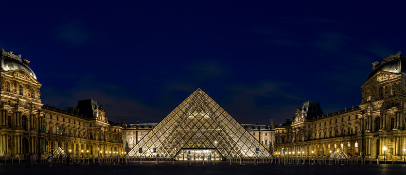 Louvre Museum illuminated at night in Paris, France, with the iconic glass pyramid and historic palace architecture reflected in the courtyard