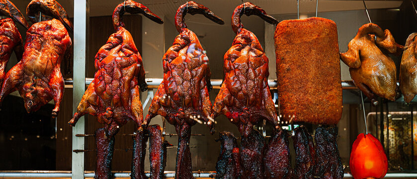Traditional Cantonese roast meats hanging in glass showcase window of Chinese restaurant.