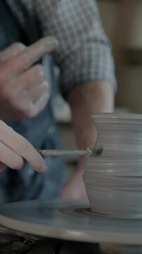 Close-up of people adult and child decorating ceramic jug in pottery workshop busy with creative activity. Traditional arts and studio concept.