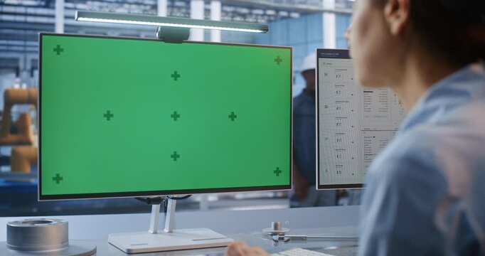 Young Female Technician Sitting at Industrial Workstation Types in Front Green Screen Display with Tracking Markers. Perfect For Compositing Customized Smart Factory Digital Interface. Industry 4.0.