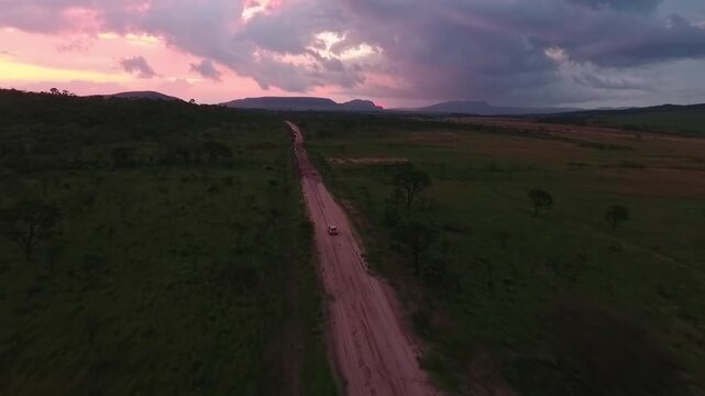 4x4 SUV travels along a dirt road in Vale Verde, Alto Paraiso de Goias, Goias, Brazil, South America, crossing the Chapada dos Veadeiros Cerrado beneath dramatic sunset clouds, drone follow tracking s
